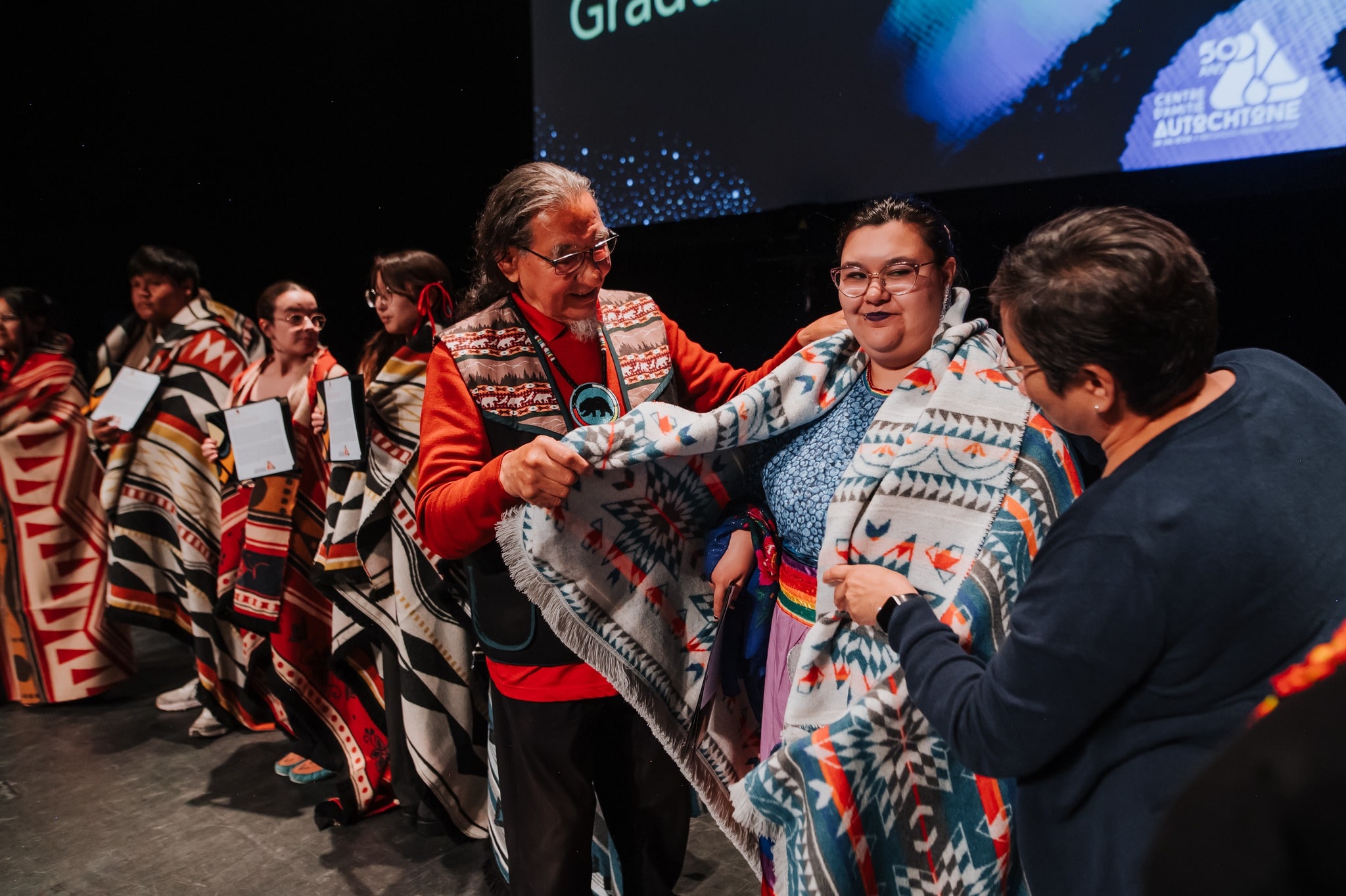 Cérémonie dans un centre d’amitié autochtone où des personnes sont honorées avec des couvertures traditionnelles.