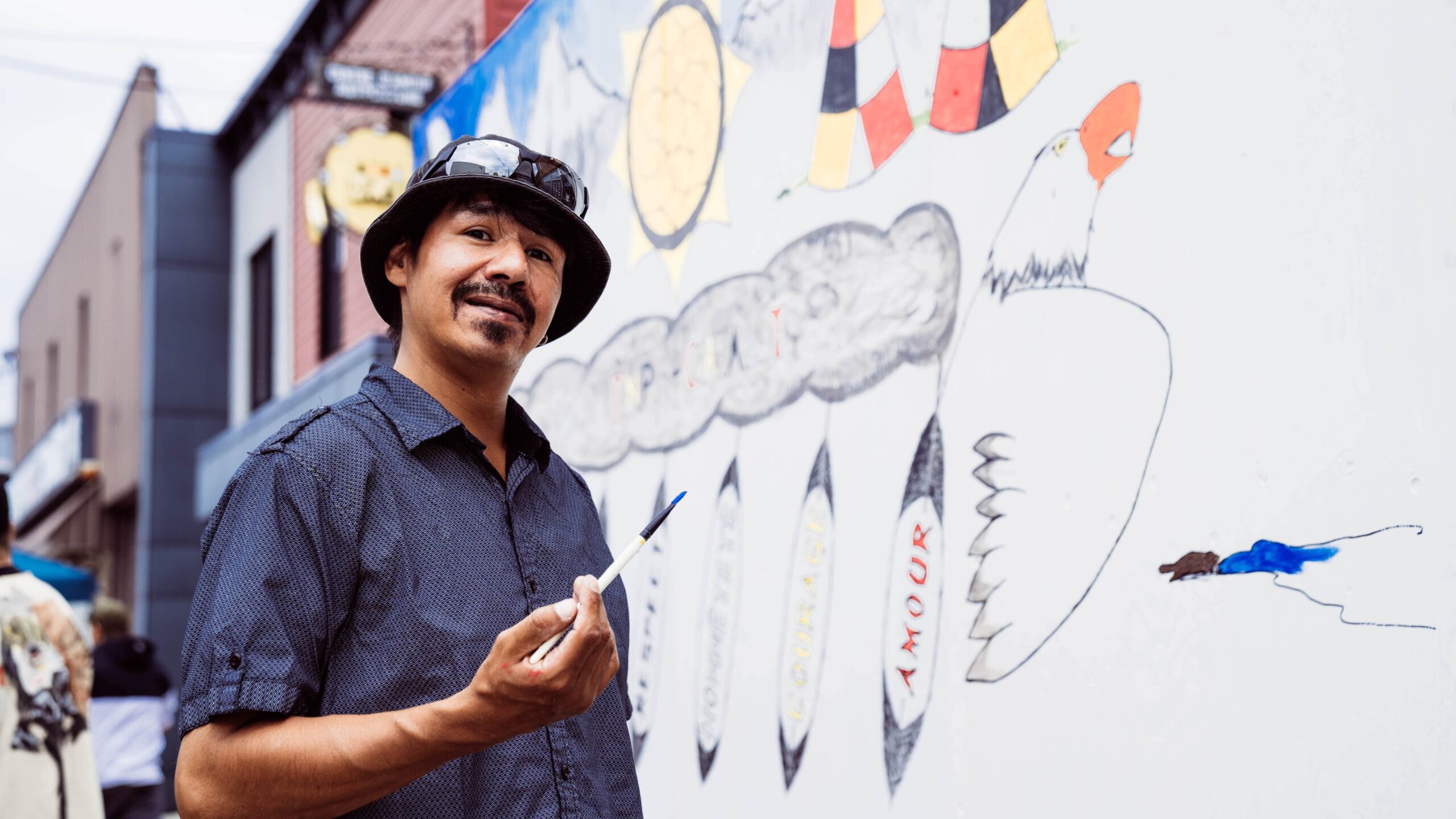 Murale avec des symboles et couleurs autochtones, dont un aigle et des plumes portant des mots comme « amour », près du Centre d’amitié autochtone Capetciwotakanik - La Tuque.