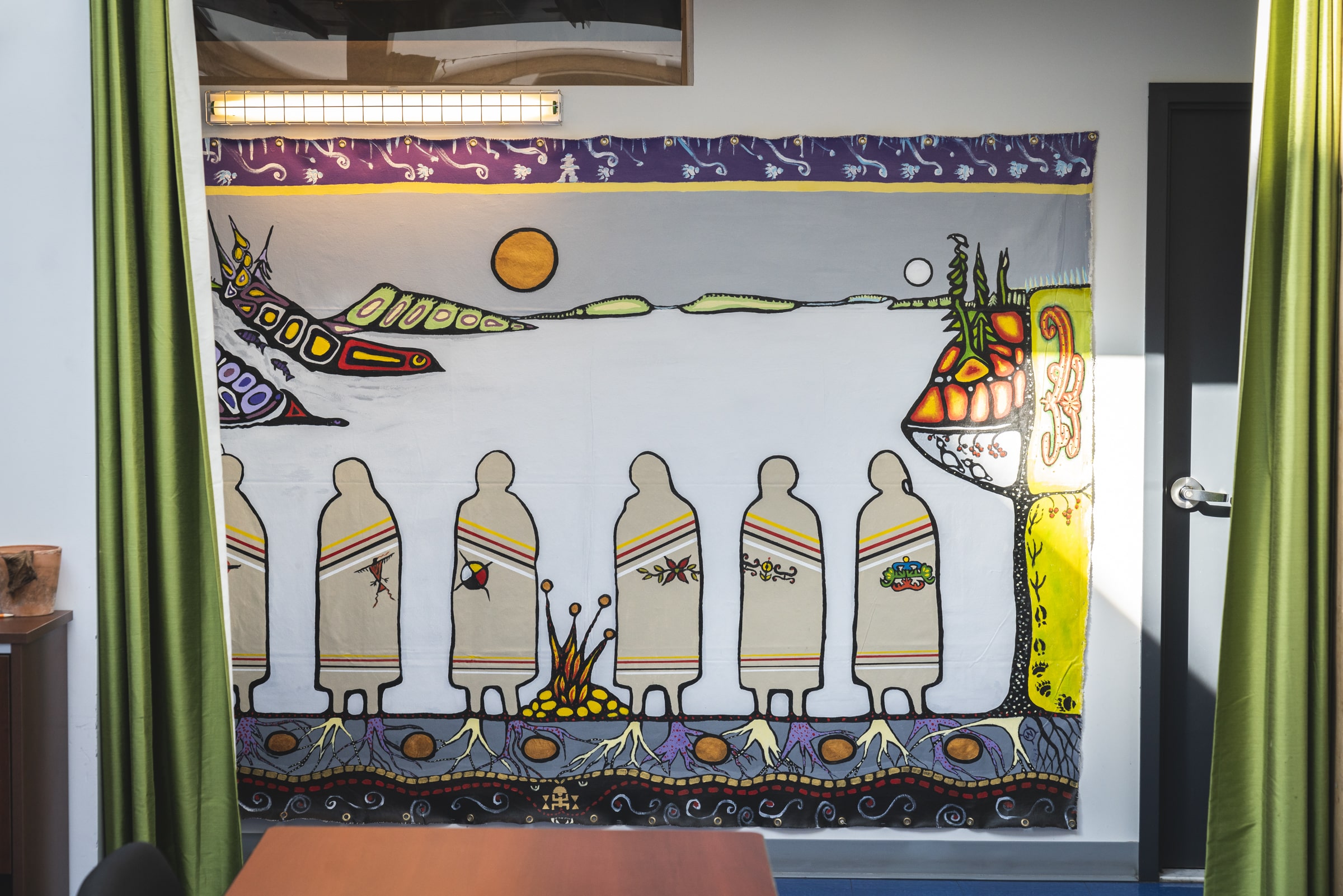 Murale intérieure dans un centre d’amitié autochtone, représentant des figures humaines symboliques et des éléments naturels inspirés de l’art autochtone.