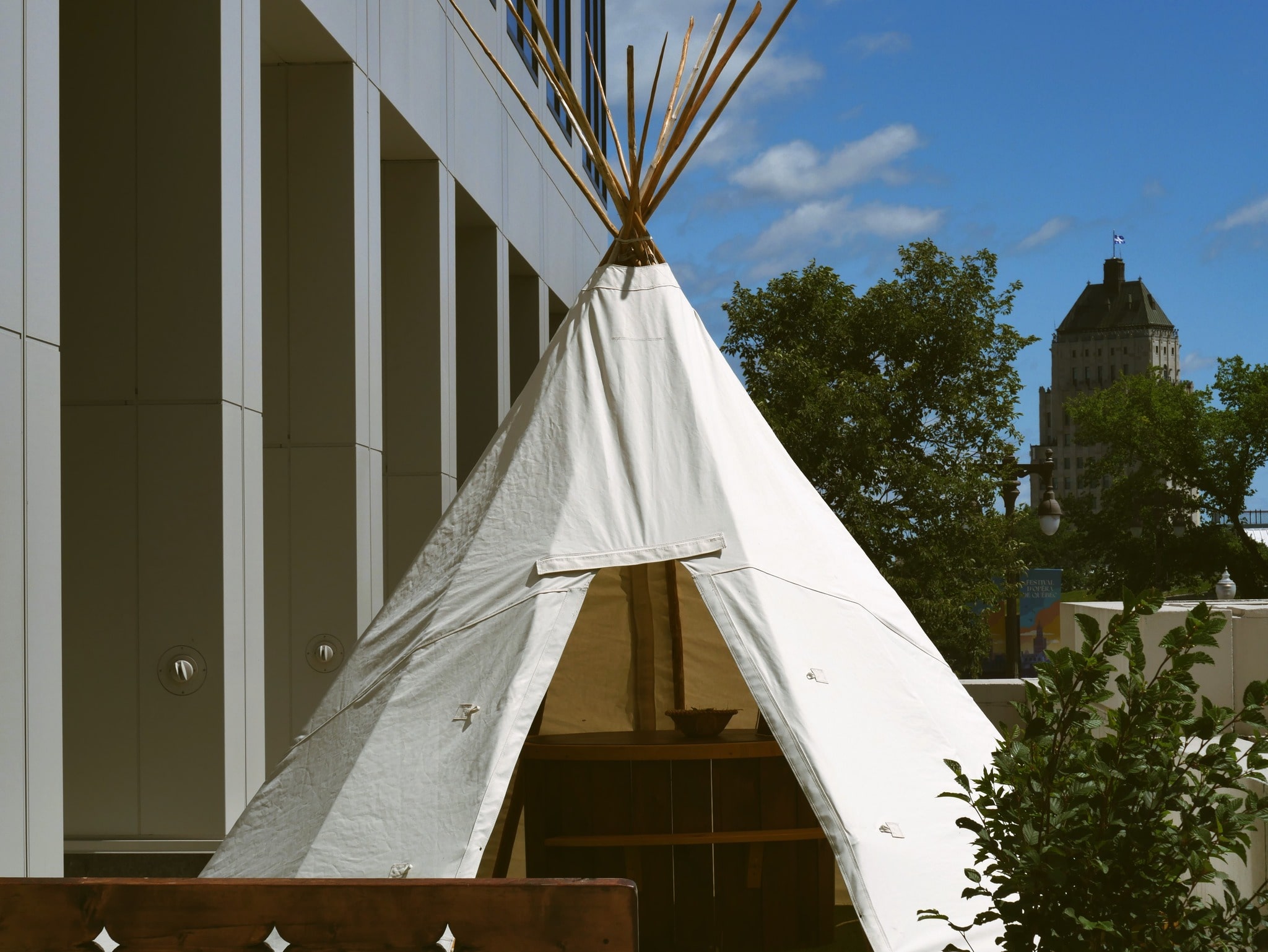 Tipi traditionnel autochtone érigé en milieu urbain, à proximité d’un bâtiment moderne.