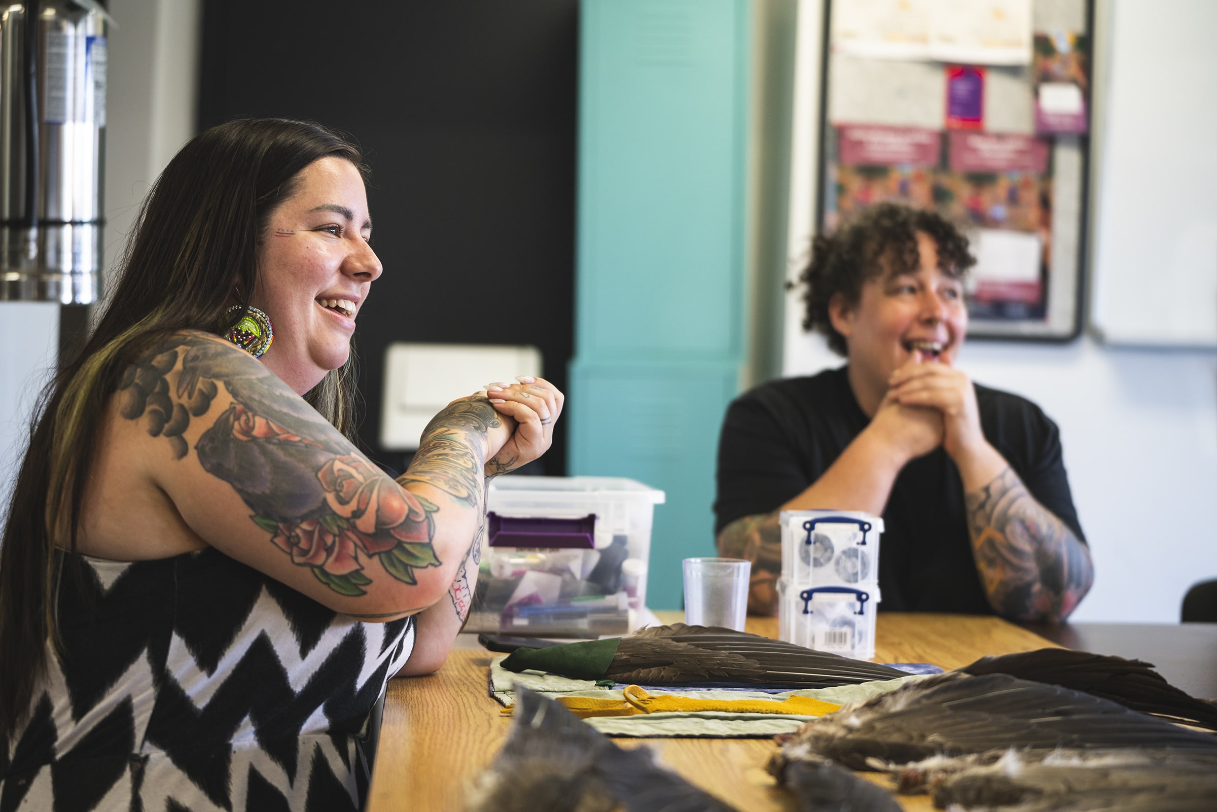 Deux personnes échangent dans le Centre d'amitié Montréal Autochtone autour d’objets culturels autochtones disposés sur une table, illustrant le dialogue et la valorisation des traditions.