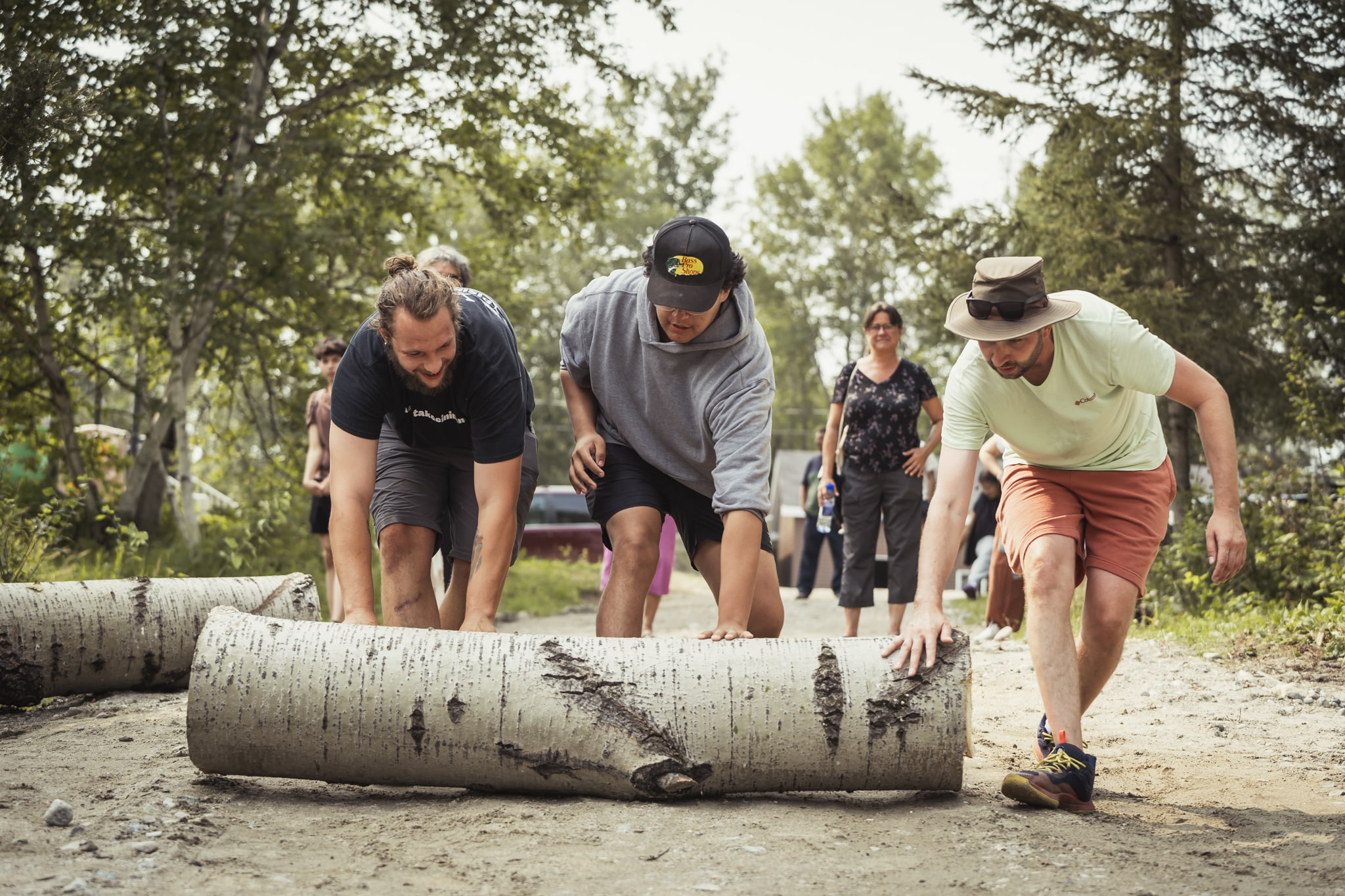 Activité communautaire en plein air : des participants déplacent des troncs d’arbre lors d’un atelier collaboratif en forêt.