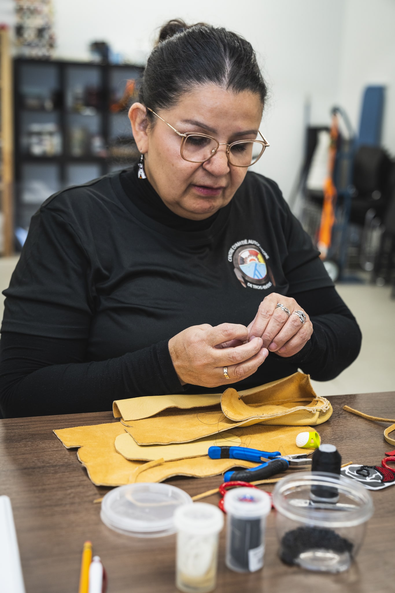 Personne réalisant un travail d’artisanat traditionnel dans un centre d’amitié autochtone, entourée de matériaux et outils.