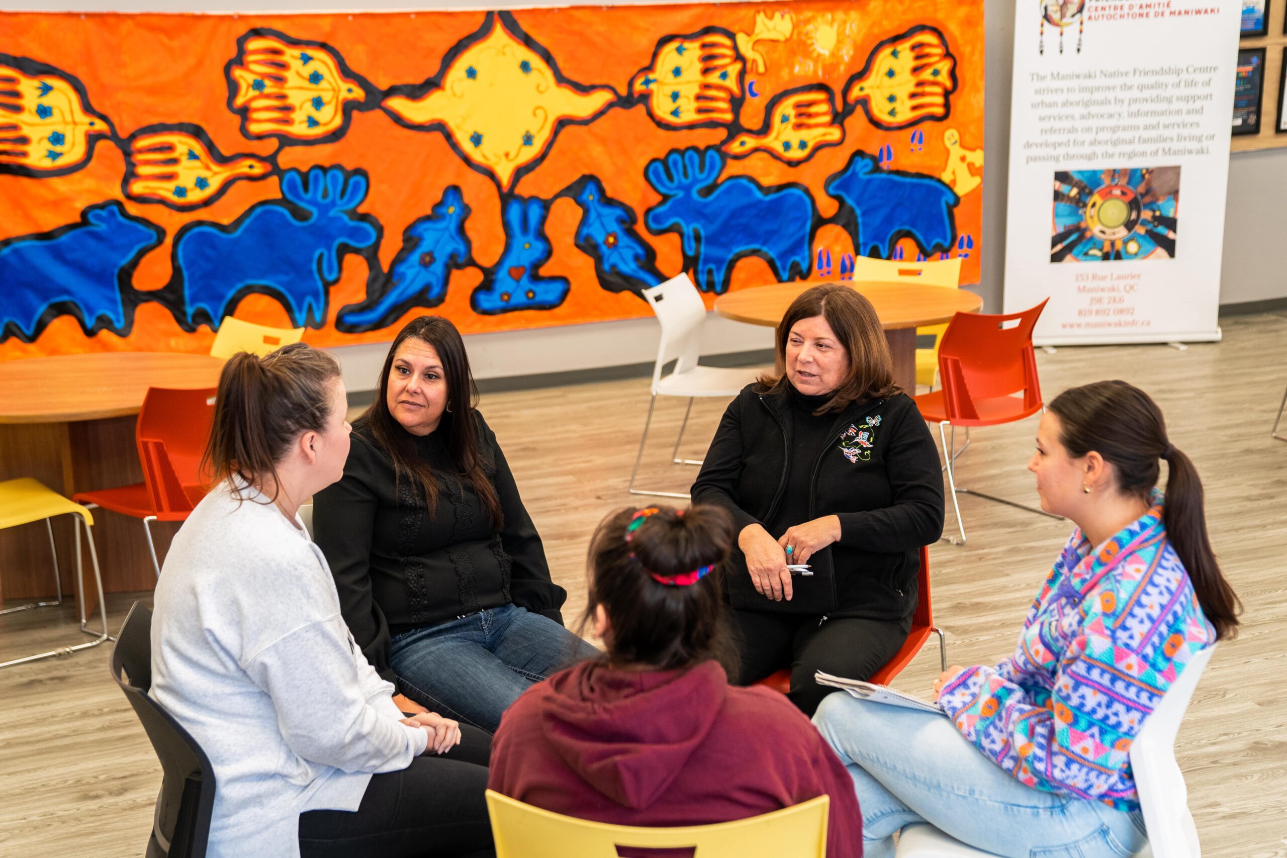 Employés réunis en cercle dans un Centre d’amitié autochtone, devant une murale colorée.