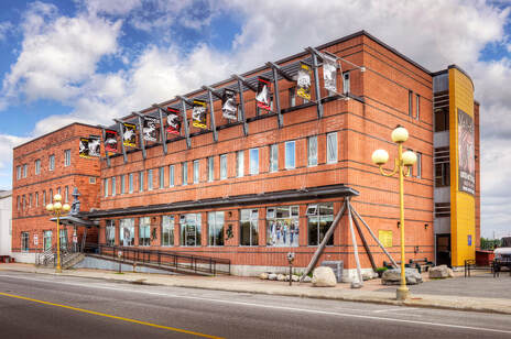 Façade extérieure du Centre d’amitié autochtone de Val-d’Or avec œuvres autochtones en vitrine, drapeaux et entrée accessible.