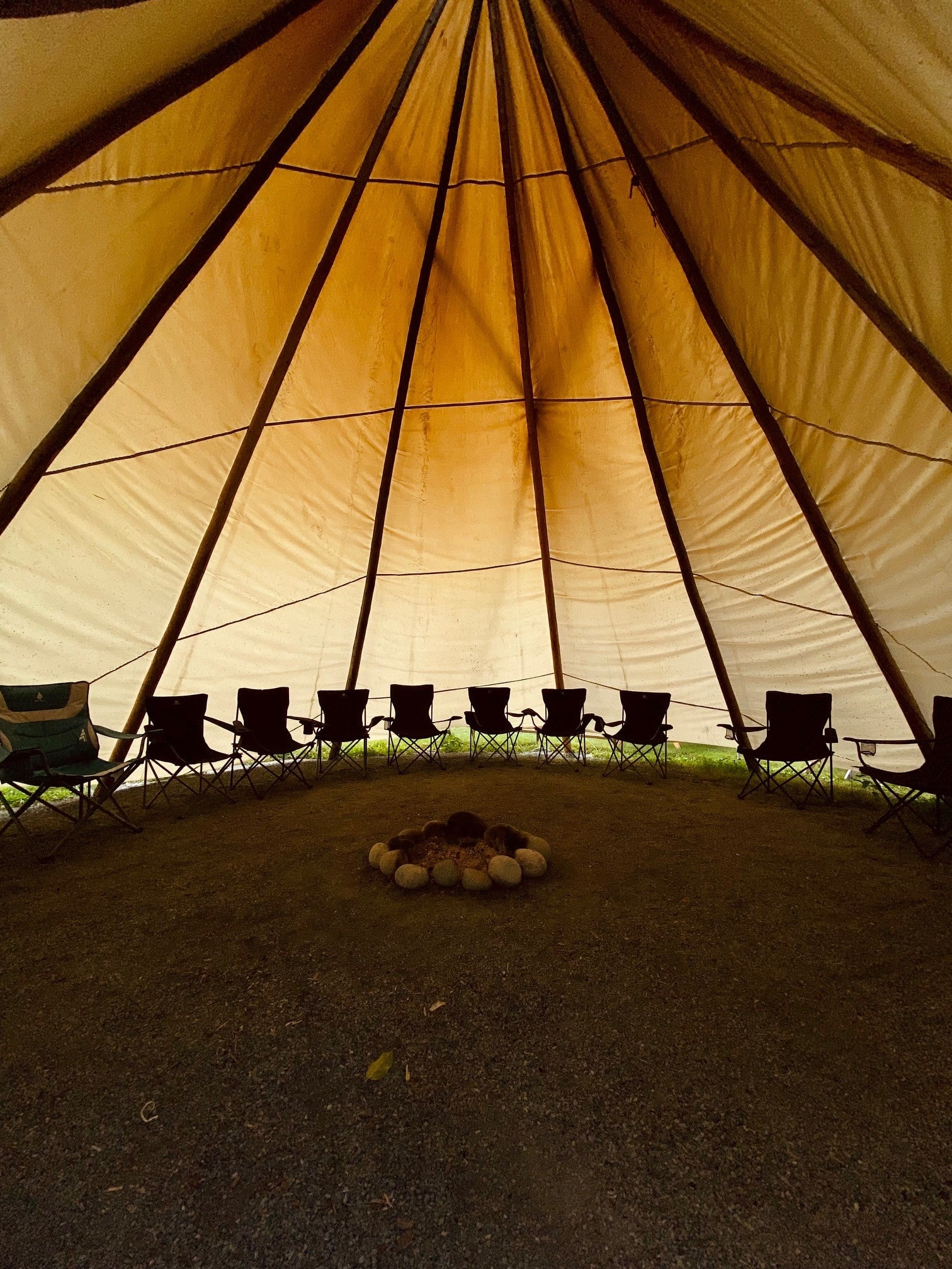Intérieur d’un tipi avec foyer central et chaises disposées en cercle pour un rassemblement.