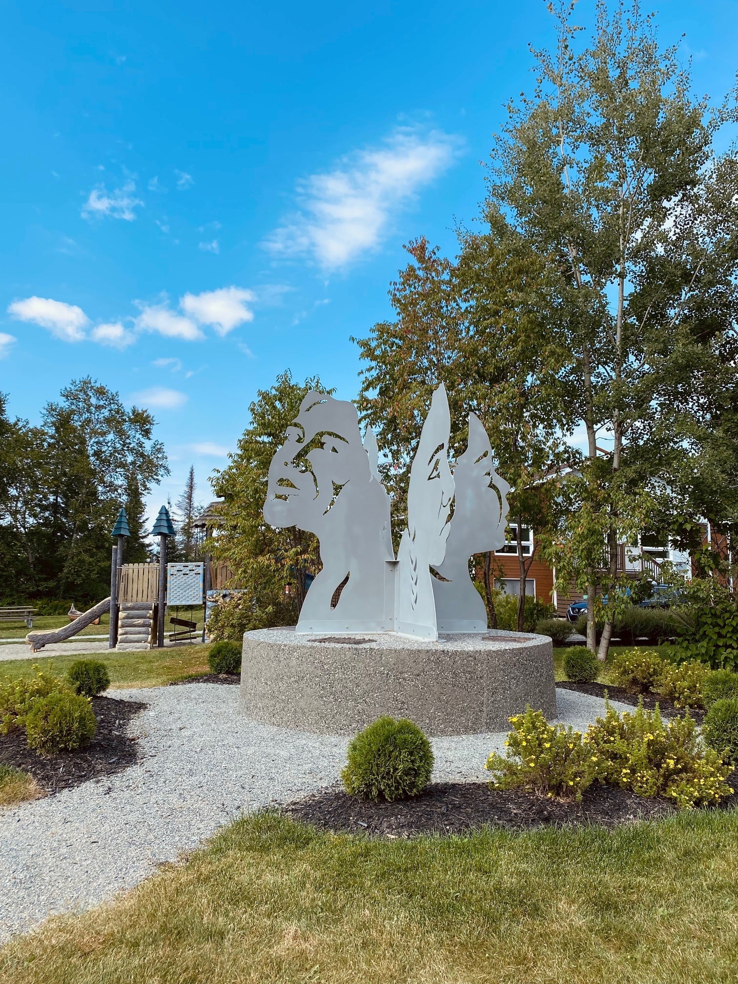Sculpture extérieure représentant des visages au site culturel Kinawit à Val-d’Or, entourée d’un aménagement paysager.