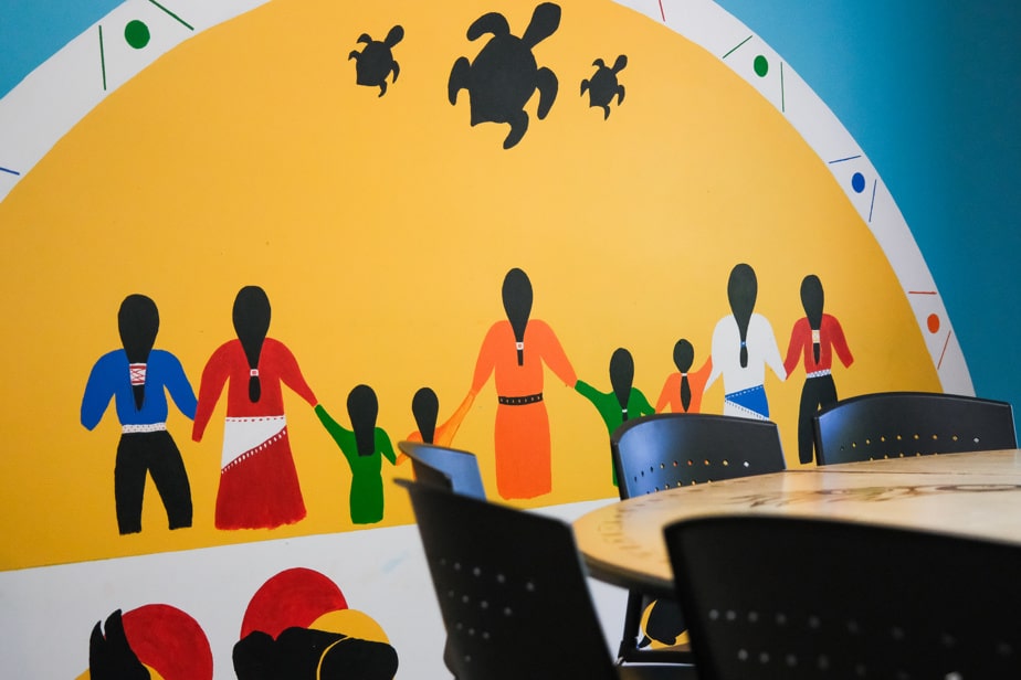 Murale intérieure représentant des personnes se tenant la main sous des silhouettes de tortues, dans un espace communautaire d’un Centre d’amitié autochtone.