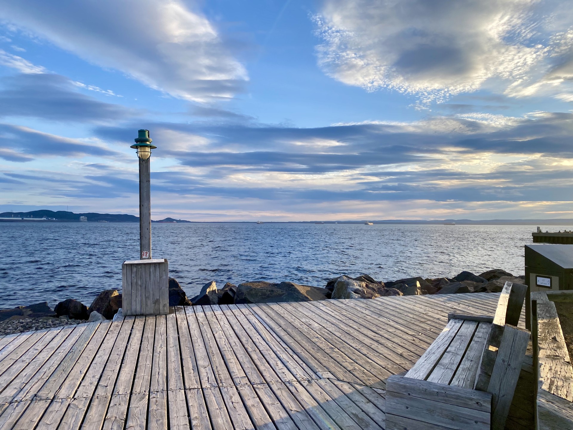 Vue du port de Sept-Îles avec digue rocheuse, passerelle en bois et horizon marin sous un ciel nuageux.