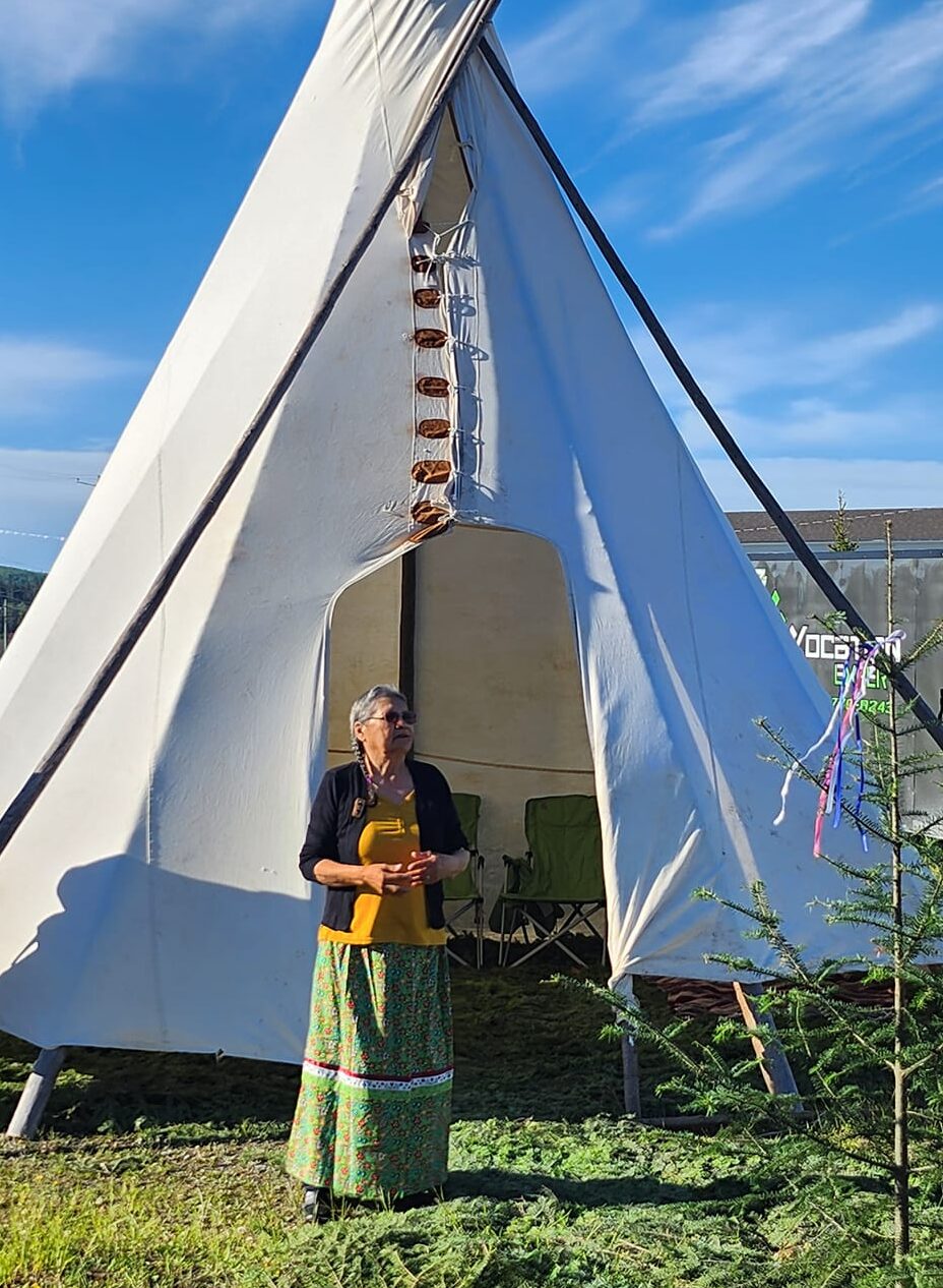 Tipi traditionnel installé sur un terrain gazonné en milieu urbain, avec deux personnes autochtones à proximité.