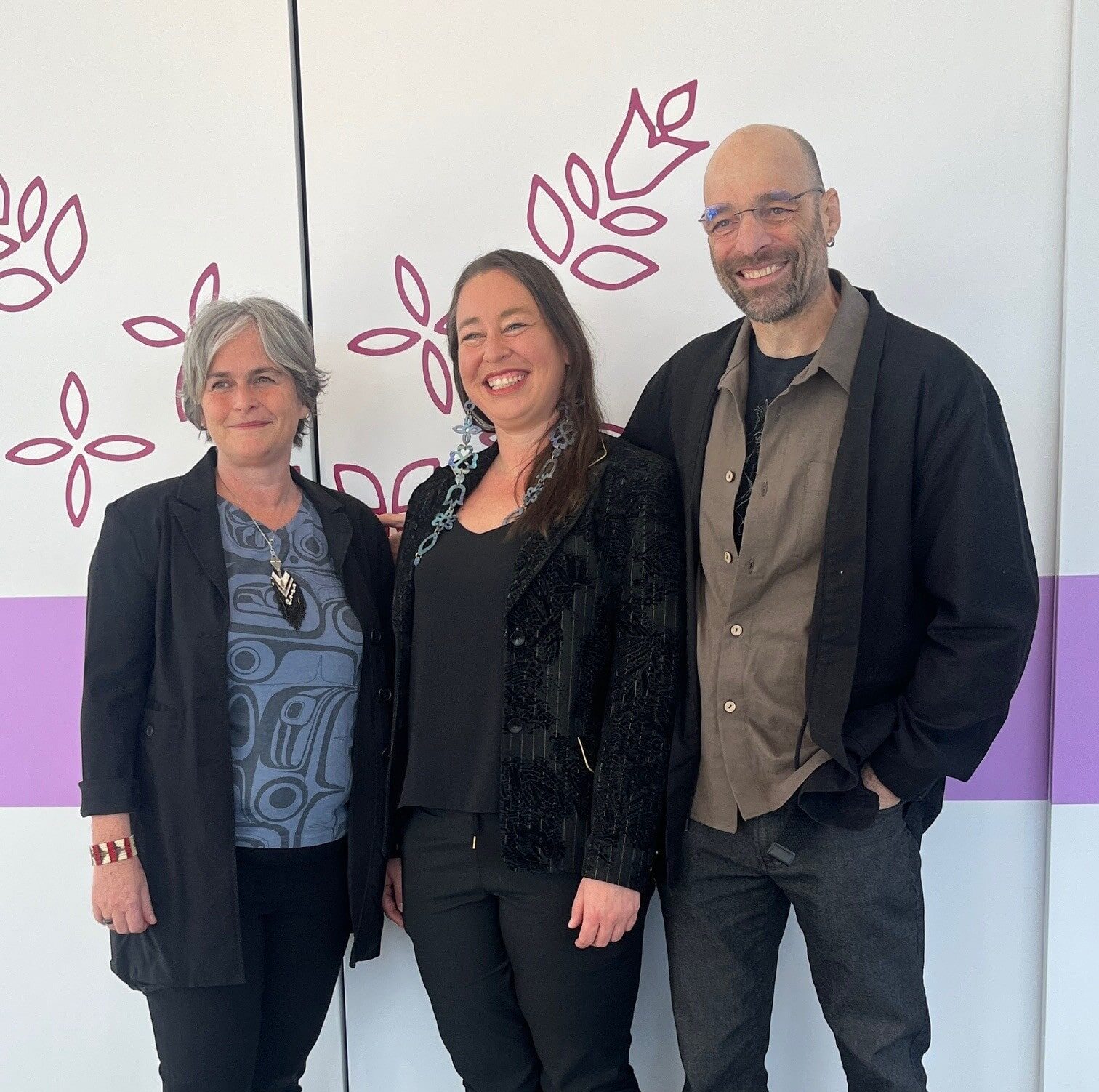 Trois personnes posant devant un mur décoré de motifs floraux violets lors de l’inauguration du Centre d’amitié autochtone de Lanaudière, dans le cadre d’une campagne de financement