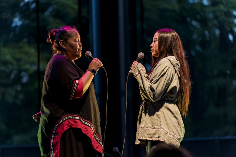 Deux personnes interprétant un chant de gorge inuit sur scène avec des microphones lors d’un événement culturel.