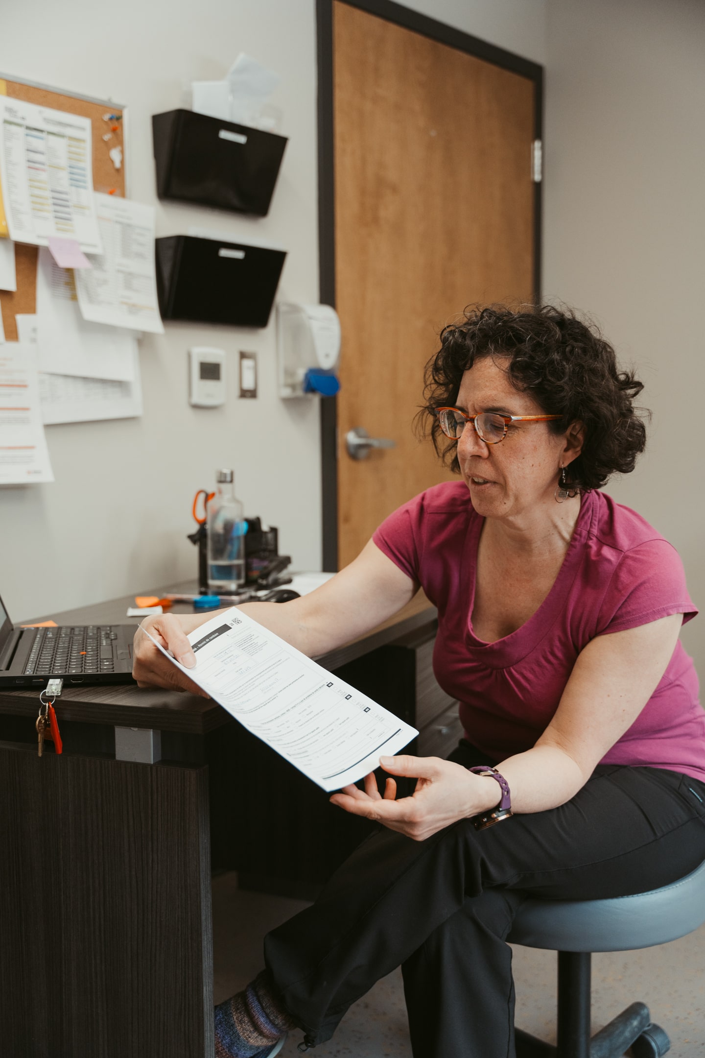 Professionnel de la santé dans un bureau d’un Centre d’amitié autochtone, tenant un document et travaillant sur un ordinateur pour offrir des services communautaires en milieu urbain.