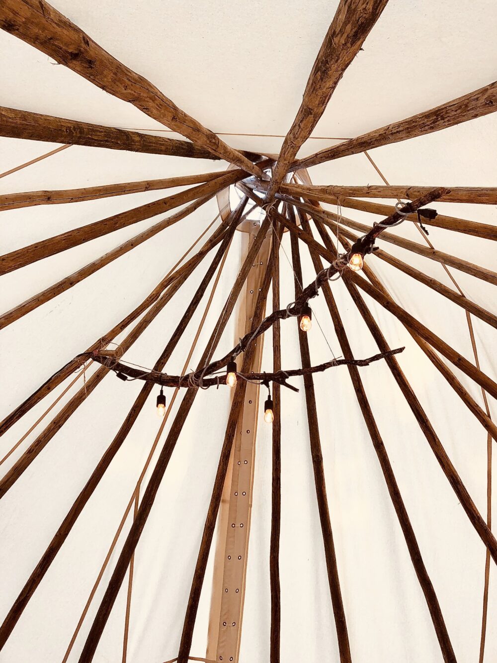 Vue intérieure d’un tipi traditionnel avec des perches en bois et une toile aux teintes chaudes, illustrant la culture et l’art autochtone.