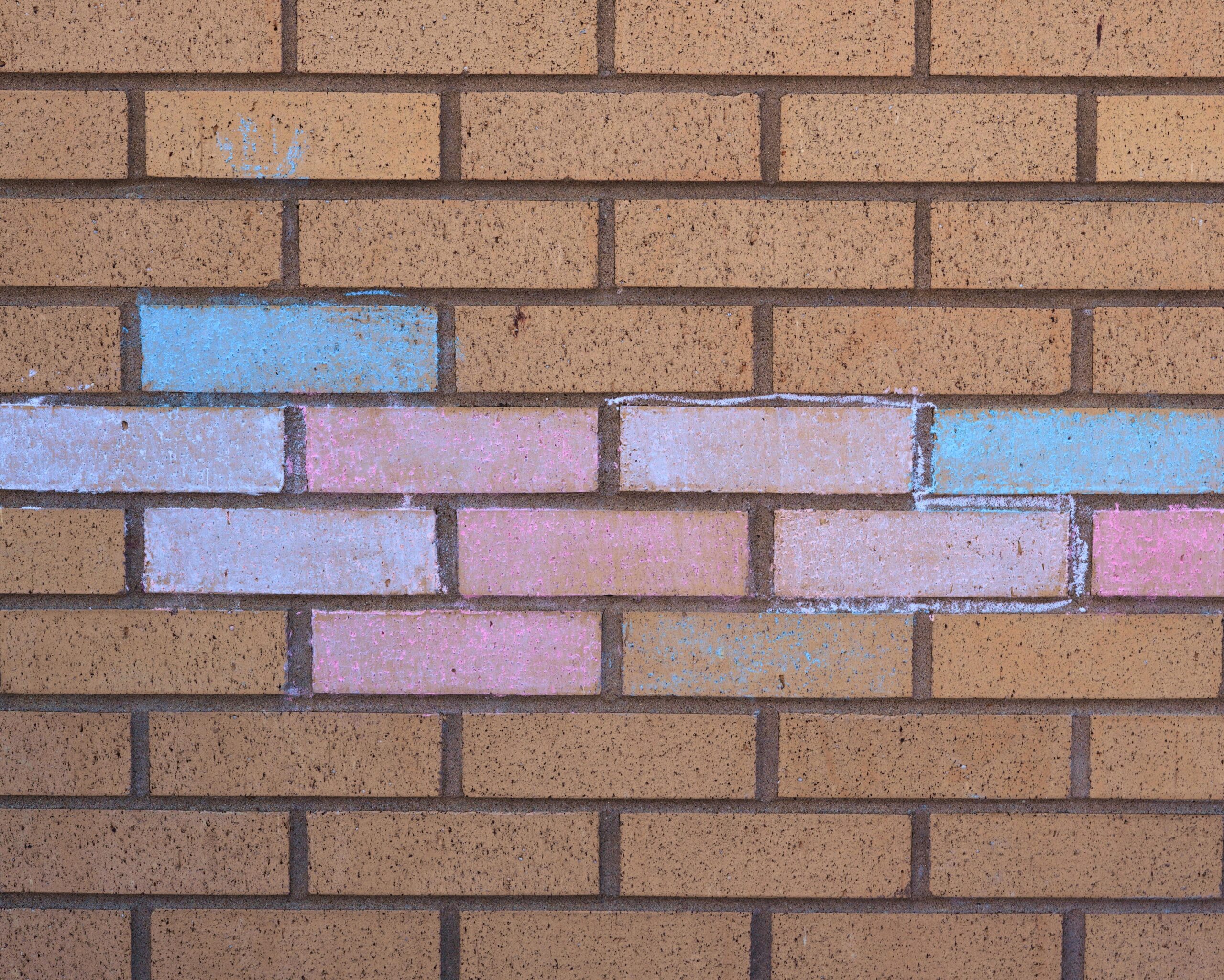 Mur de briques avec des traces de craie colorée en bleu, rose et blanc 