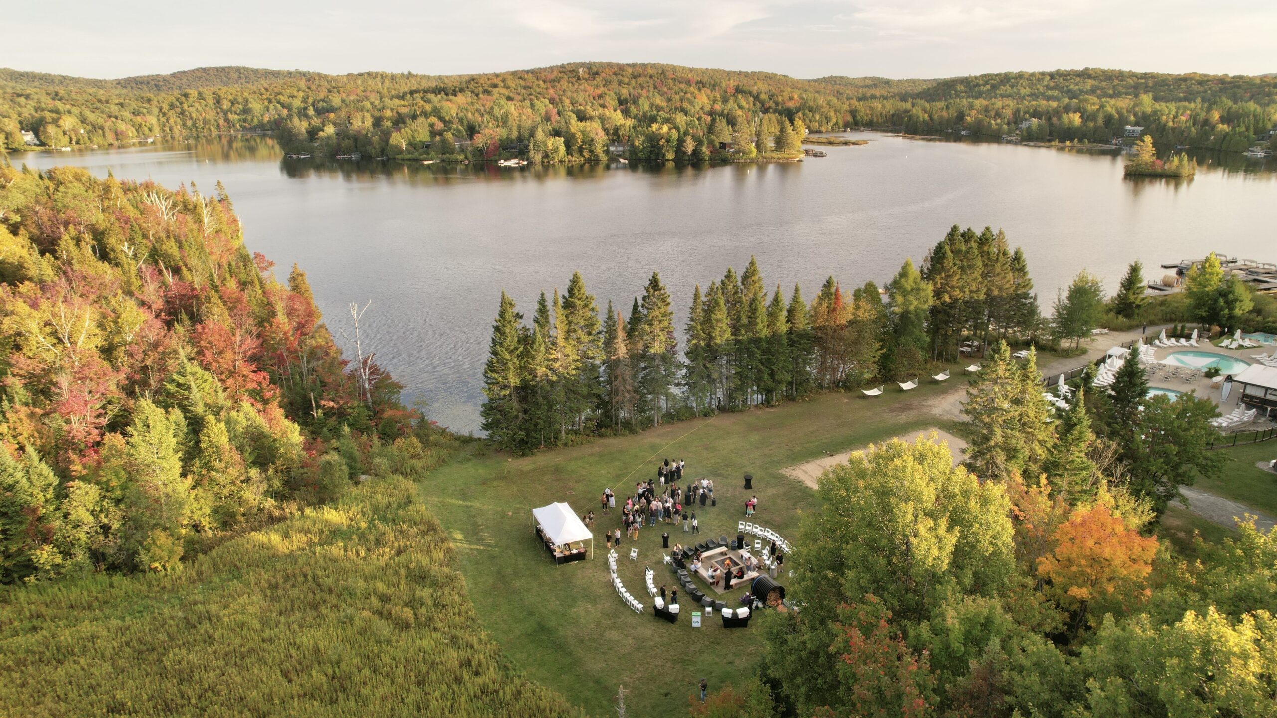 Vue aérienne d’un rassemblement en plein air près d’un lac entouré de forêt aux couleurs automnales – Regroupement des centres d’amitié autochtones du Québec (RCAAQ)