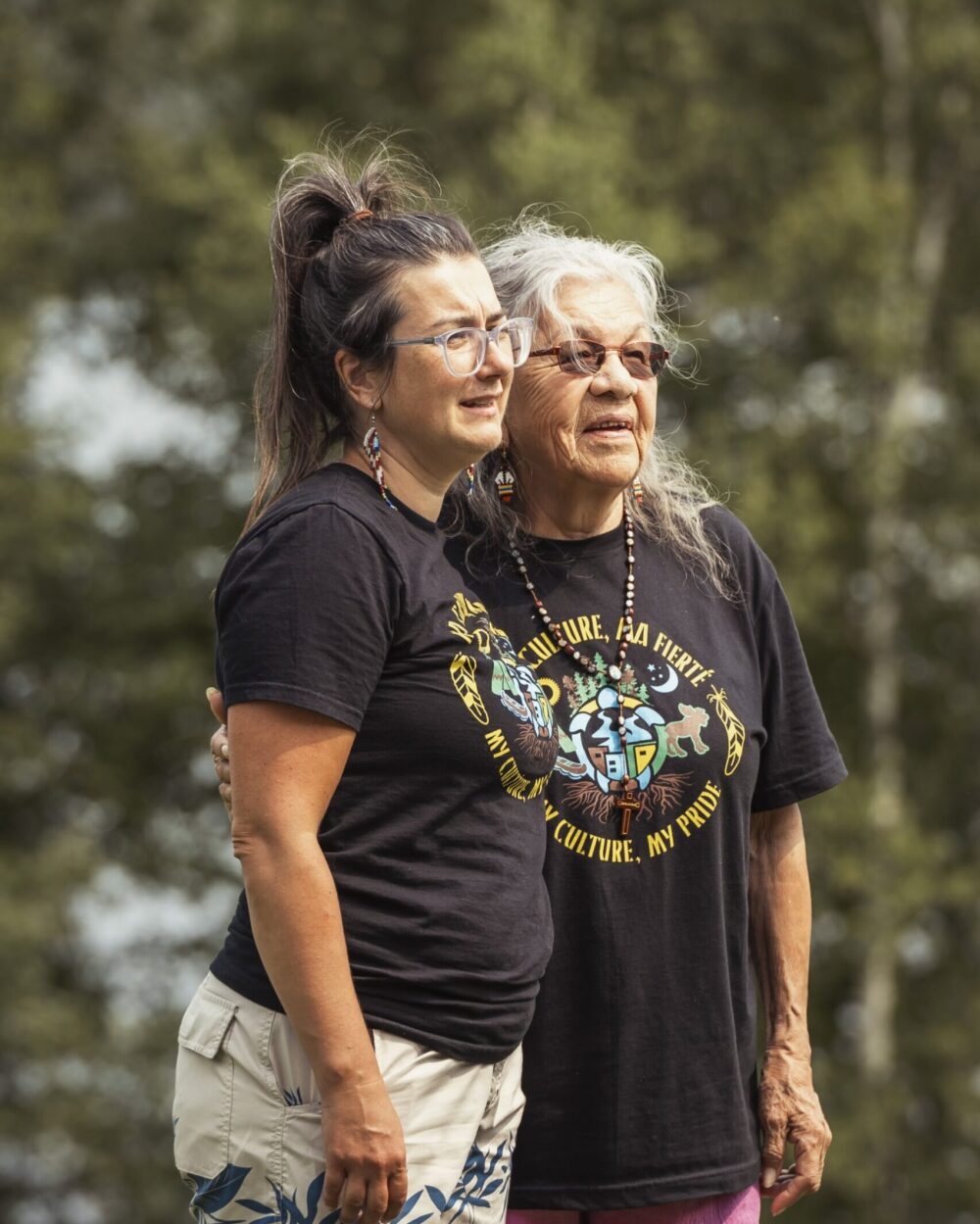 Deux personnes portant des t-shirts avec motifs culturels autochtones, illustrant la fierté et la transmission des traditions