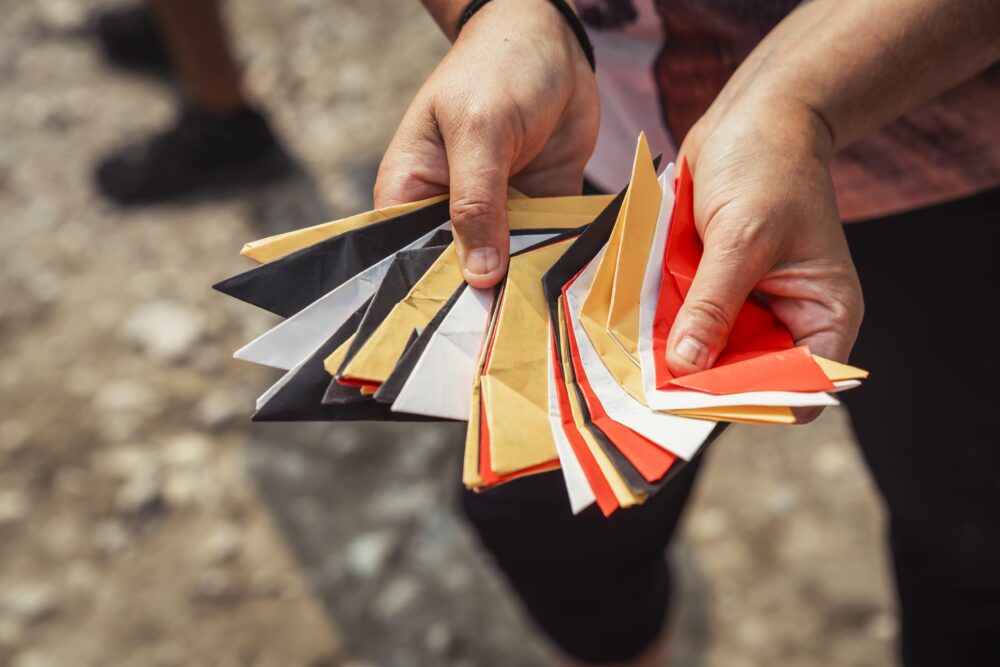Main tenant plusieurs pièces de papier pliées aux couleurs rouge, blanc, noir et jaune lors d’un atelier culturel autochtone