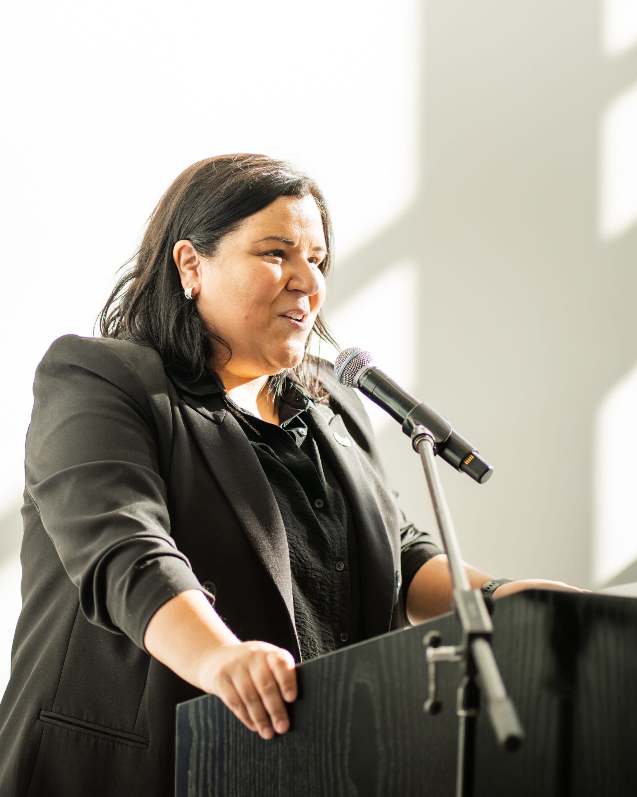 Personne en tenue professionnelle prenant la parole à un podium avec un micro lors d’un événement officiel.