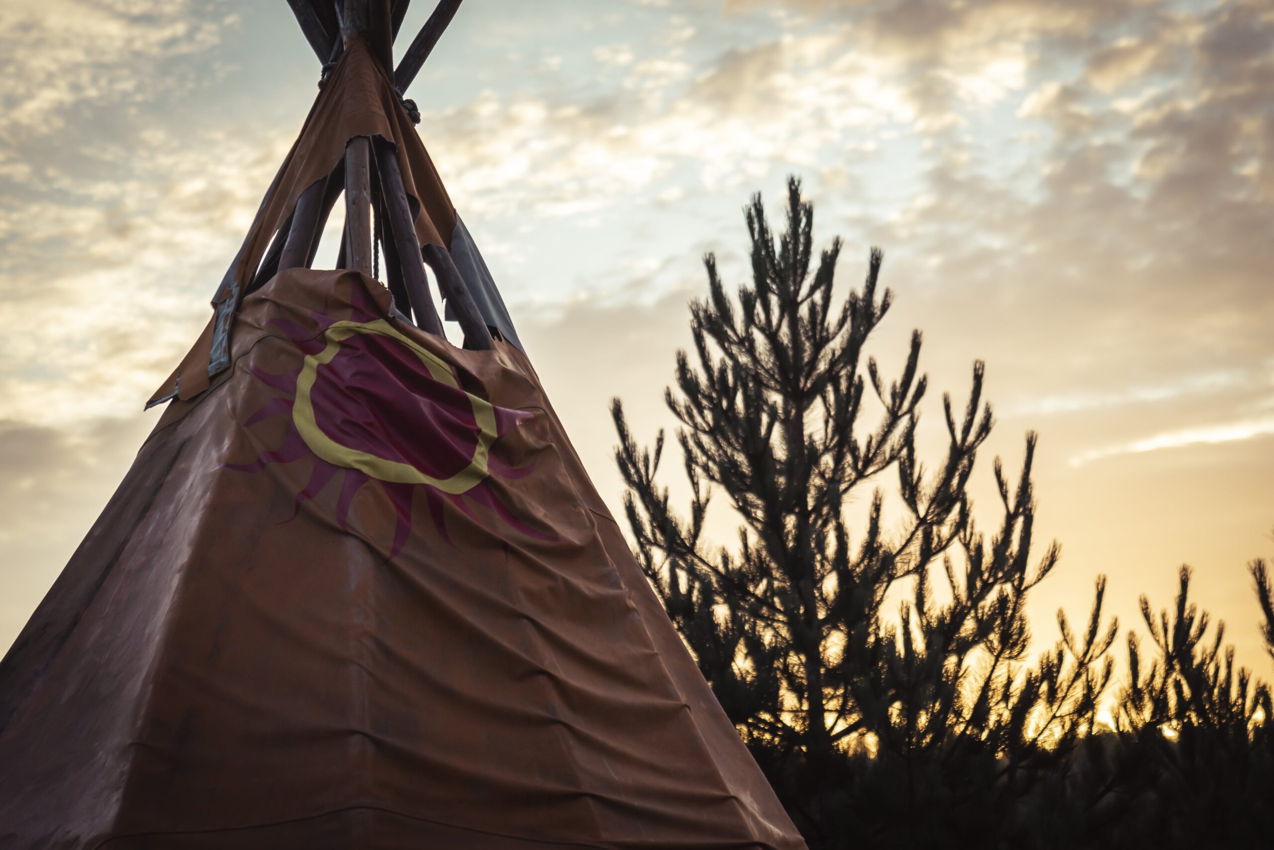 Tipi traditionnel au coucher du soleil avec un arbre en arrière-plan lors du rassemblement jeunesse du RCAAQ
