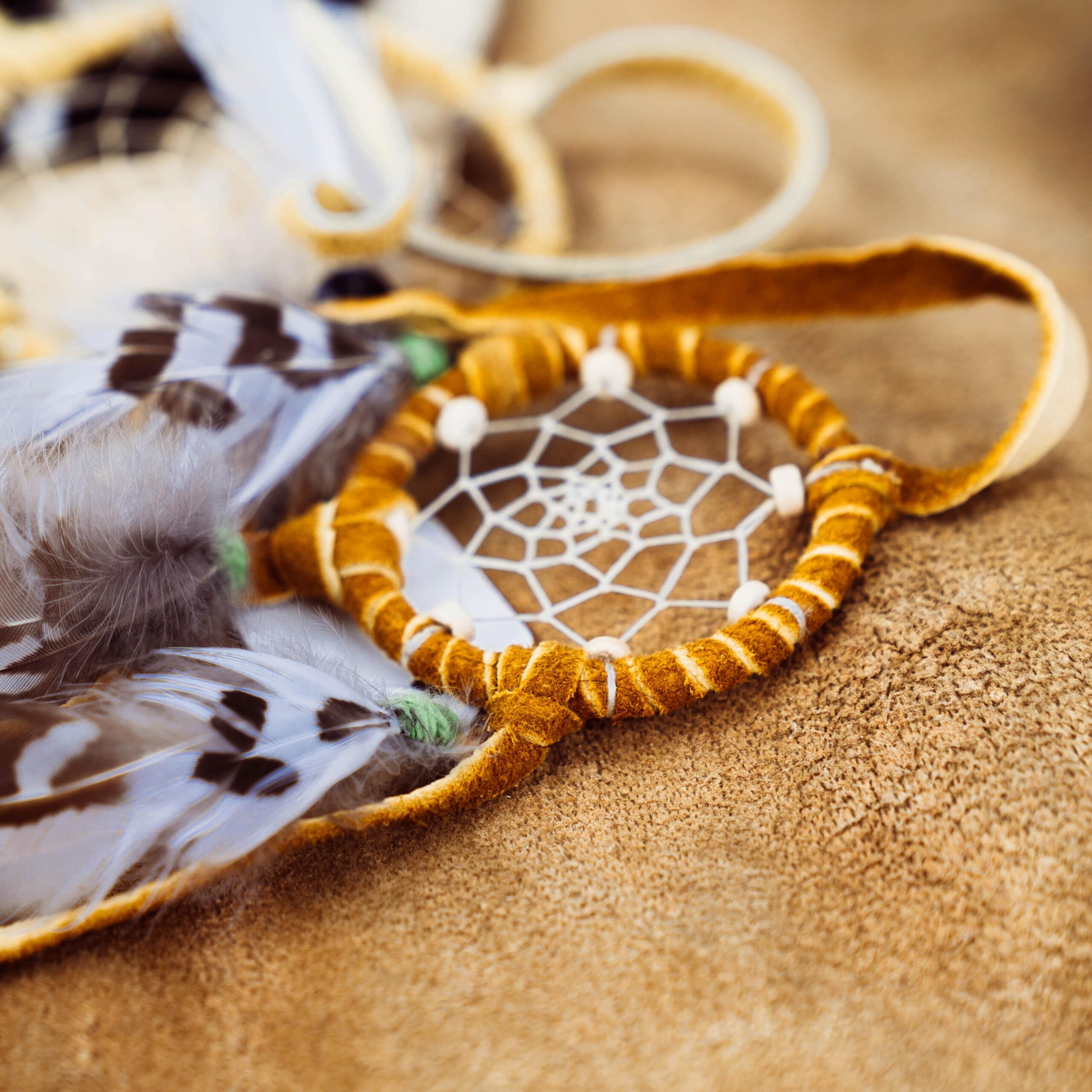 Capteur de rêves traditionnel avec plumes et perles, posé sur une surface en cuir.