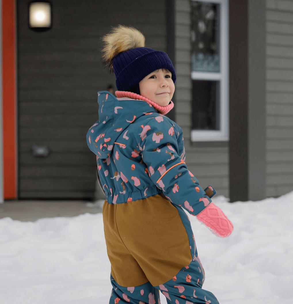 Enfant vêtu d’un habit d’hiver coloré avec tuque et mitaines, jouant dehors dans la neige devant un bâtiment résidentiel d’un milieu de vie de la SIRCAAQ.