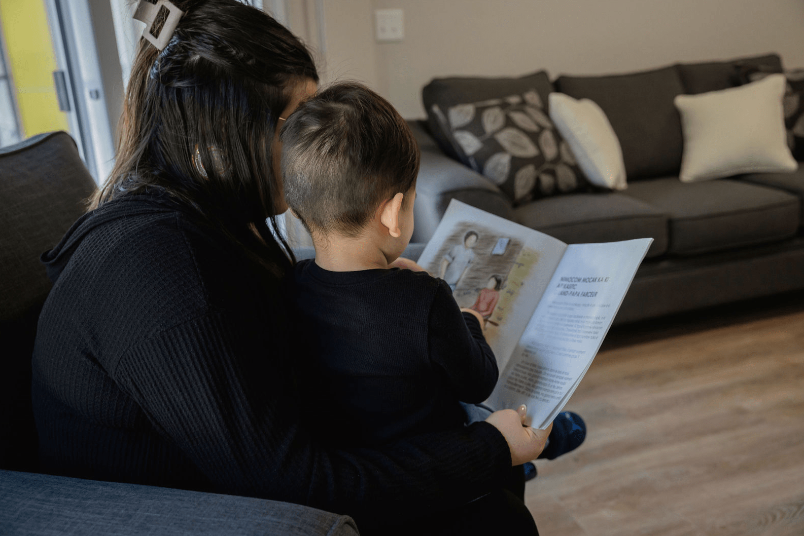Personne assise sur un canapé lisant un livre illustré à un enfant dans un logement chaleureux d’un milieu de vie de la SIRCAAQ.