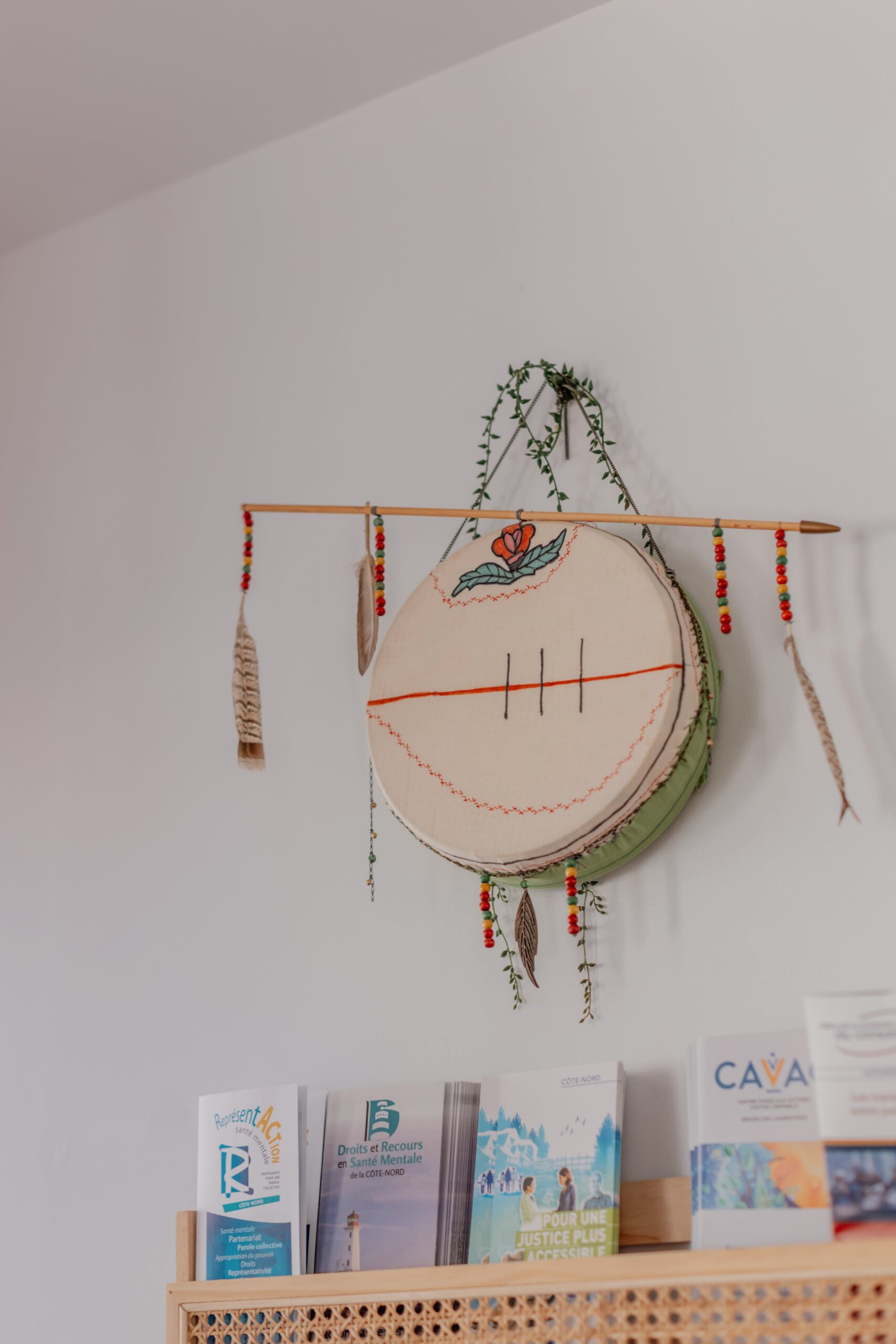 Tambour autochtone décoratif suspendu au mur avec plumes et perles, au-dessus d’un présentoir de brochures dans un Centre d’amitié